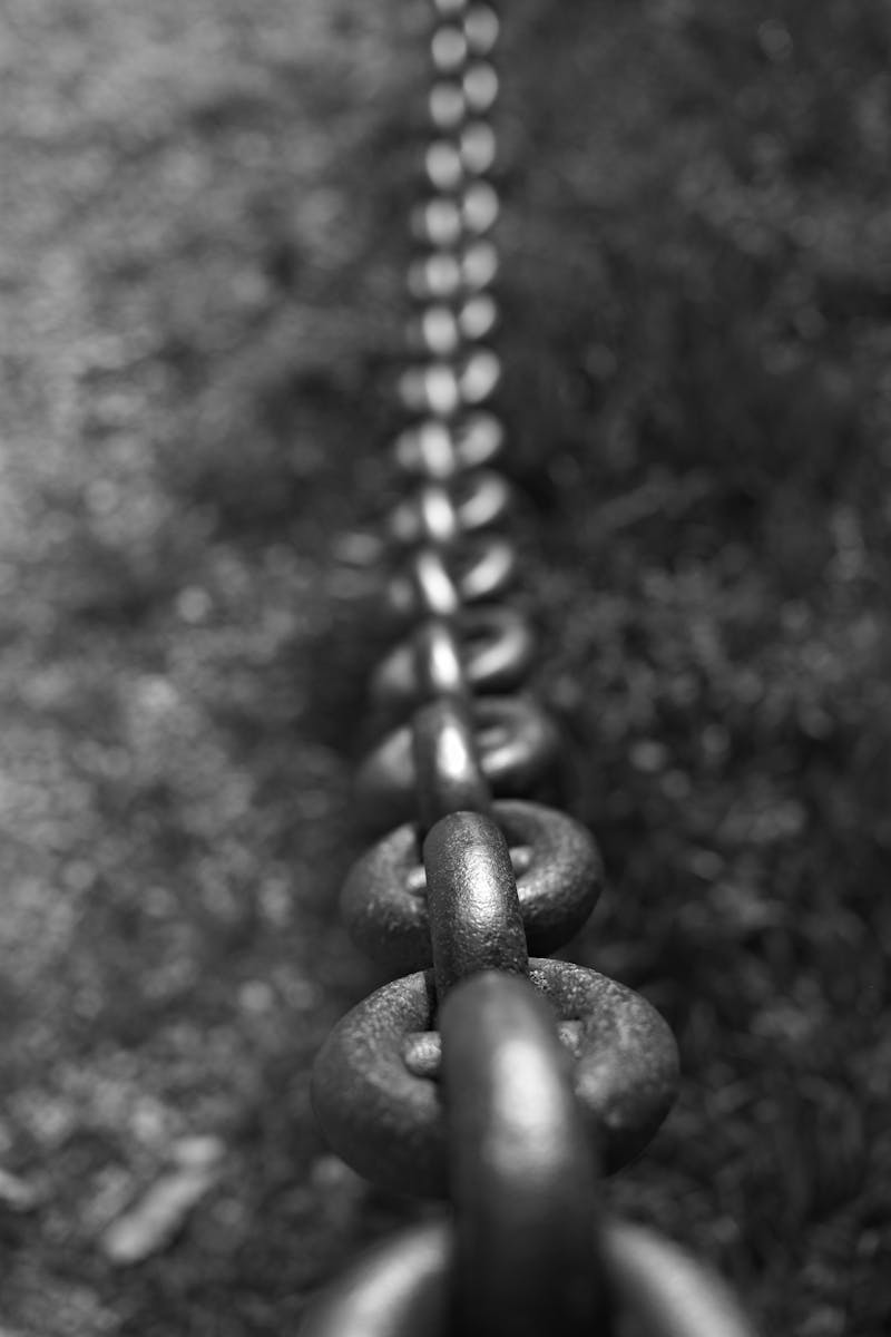 Black and white photo of a strong iron chain fading into the distance outdoors.